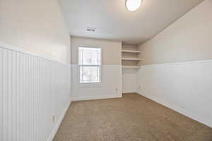 Spare room with light colored carpet, a textured ceiling, and a wainscoted wall