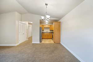 Kitchen with a chandelier, decorative light fixtures, vaulted ceiling, light carpet, and appliances with stainless steel finishes