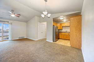 Kitchen with vaulted ceiling, light carpet, open floor plan, decorative light fixtures, and freestanding refrigerator