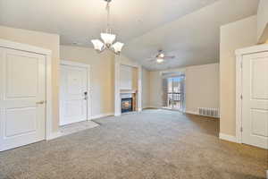 Unfurnished living room featuring light colored carpet, a fireplace, a chandelier, and vaulted ceiling