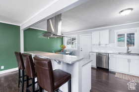 Kitchen featuring white cabinetry, range hood, a kitchen bar, stainless steel dishwasher, and light stone countertops