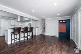 Kitchen featuring dark wood-type flooring, a kitchen bar, recessed lighting, ventilation hood, and light countertops