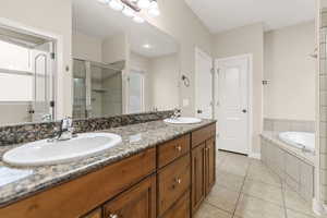 Full bath with double vanity, light tile patterned flooring, a garden tub, and a stall shower