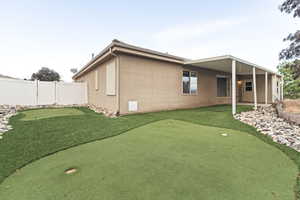 Back of house with a putting green, a patio area, and stucco siding