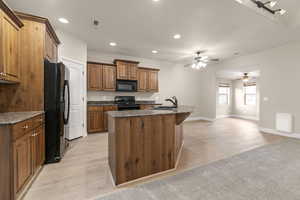 Kitchen featuring black appliances, recessed lighting, an island with sink, light wood-style floors, and dark stone countertops