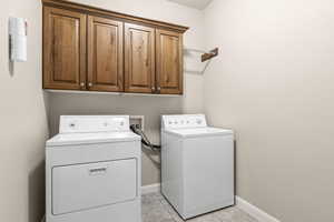 Washroom with cabinet space, light tile patterned flooring, and washer and clothes dryer