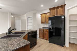 Kitchen featuring built in shelves, black appliances, brown cabinetry, light wood-style floors, and recessed lighting