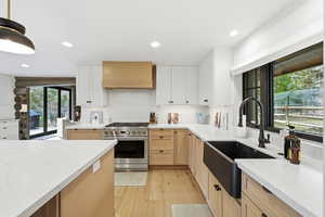 Kitchen featuring high end stove, light brown cabinets, light wood finished floors, light stone counters, and custom range hood