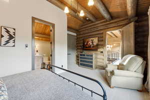 Carpeted bedroom with wood ceiling, a chandelier, rustic walls, and connected bathroom