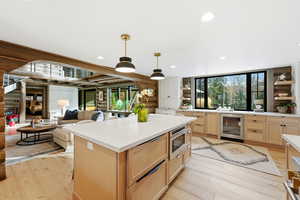 Kitchen featuring light brown cabinetry, wine cooler, open shelves, hanging light fixtures, and light wood-style flooring