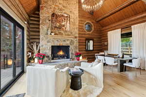 Living area with a fireplace, log walls, light wood-style flooring, high vaulted ceiling, and a wooden ceiling with exposed beams