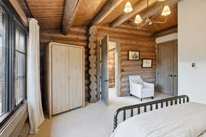 Bedroom with rustic walls, a wooden ceiling with exposed beams, a chandelier, and ensuite bath