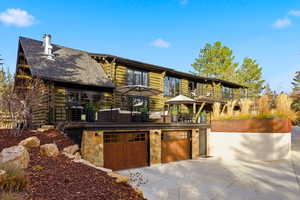 Log cabin featuring driveway, stone siding, roof with shingles, an attached garage, and log siding