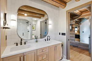 Full bathroom with double vanity, a stall shower, rustic walls, light wood-type flooring, and a wooden ceiling with exposed beams