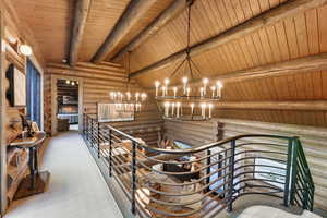 Hallway with log walls, wooden ceiling, a chandelier, and an upstairs landing