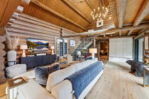 Living area with a wooden ceiling with exposed beams, stairs, light wood-type flooring, rustic walls, and high vaulted ceiling