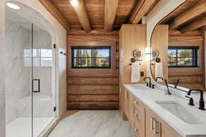 Full bathroom featuring rustic walls, a wood ceiling with exposed beams, double vanity, a marble finish shower, and light marble finish floors