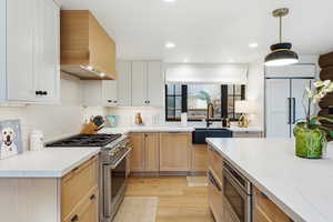 Kitchen with built in appliances, light stone counters, light wood-style floors, hanging light fixtures, and recessed lighting