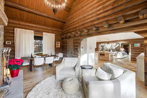 Living room with high vaulted ceiling, a wood ceiling with exposed beams, arched walkways, log walls, and a chandelier