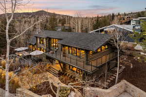 Back of house at dusk with log siding, a shingled roof, and a deck