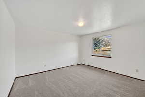 Carpeted spare room with a textured ceiling and baseboards