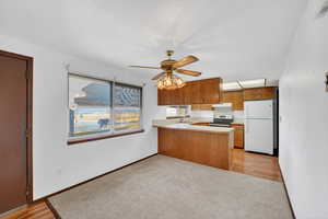 Kitchen with brown cabinetry, light countertops, freestanding refrigerator, a peninsula, and light colored carpet