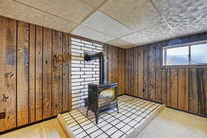 Detailed view of a wood stove, wood walls, carpet flooring, and a drop ceiling