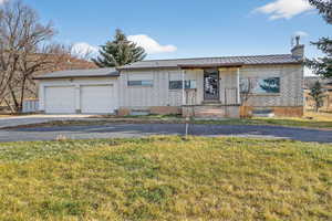 Ranch-style house featuring a metal roof, a chimney, a front yard, driveway, and an attached garage