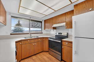 Kitchen with freestanding refrigerator, stainless steel electric range oven, brown cabinetry, light countertops, and light wood-type flooring