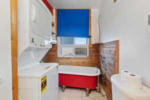 Full bathroom featuring a freestanding tub, estacked washer and dryer, and light tile patterned floors