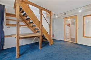 Finished basement featuring dark carpet, stairway, and track lighting