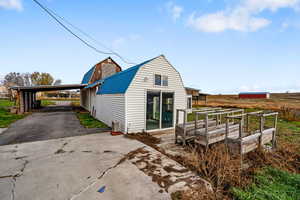 View of property exterior with a gambrel roof, driveway, a wooden deck, a metal roof, and a carport