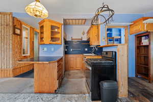 Kitchen featuring range with gas stovetop, glass insert cabinets, a kitchen bar, brown cabinetry, and wooden walls