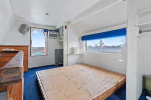 Unfurnished bedroom with dark carpet, multiple windows, and an AC wall unit