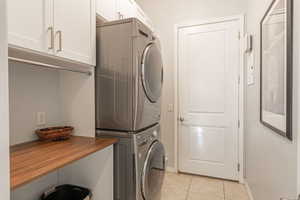 Washroom featuring light tile patterned flooring, estacked washer and dryer, and cabinet space