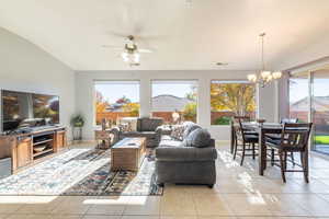 Living area with light tile patterned flooring, vaulted ceiling, ceiling fan, and a chandelier