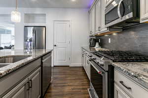 Kitchen with stainless steel appliances, light stone countertops, gray cabinetry, dark wood-type flooring, and pendant lighting