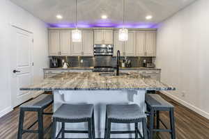 Kitchen featuring backsplash, cream cabinetry, light stone countertops, dark wood-type flooring, and recessed lighting