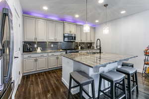 Kitchen featuring light stone countertops, a center island with sink, appliances with stainless steel finishes, tasteful backsplash, and recessed lighting