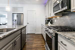 Kitchen featuring appliances with stainless steel finishes, light stone countertops, gray cabinetry, hanging light fixtures, and dark wood-style floors