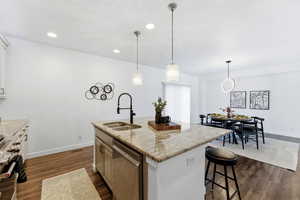 Kitchen featuring a center island with sink, light stone countertops, stainless steel appliances, decorative light fixtures, and a breakfast bar area