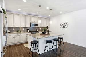 Kitchen with light stone countertops, an island with sink, a kitchen bar, hanging light fixtures, and dark wood-style flooring