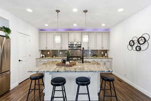 Kitchen with stainless steel appliances, light stone counters, a breakfast bar area, an island with sink, and pendant lighting