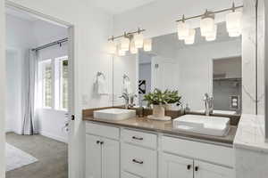 Full bath with double vanity, light colored carpet, and a spacious closet