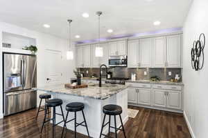 Kitchen with stainless steel appliances, light stone countertops, a kitchen breakfast bar, pendant lighting, and a kitchen island with sink