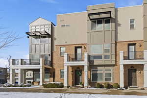 View of front of home featuring a balcony, brick siding, and stucco siding