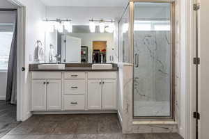 Full bathroom featuring a spacious closet, double vanity, and a marble finish shower