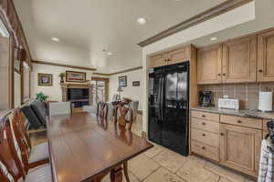 Kitchen with black fridge with ice dispenser, ornamental molding, tasteful backsplash, recessed lighting, and light stone counters
