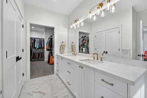 Full bathroom with a spacious closet, double vanity, and light marble finish floors