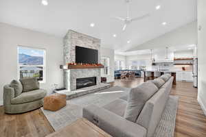 Living room with recessed lighting, light wood-type flooring, a stone fireplace, a ceiling fan, and high vaulted ceiling